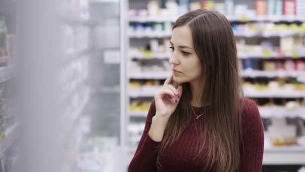 Aranyos lány a boltban azt hiszi, hogy melyik terméket vásárolni. — Stock videók