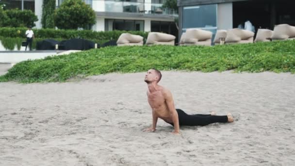 Athletic shirtless człowiek robi ćwiczenia rozciągające jogi na plaży — Wideo stockowe