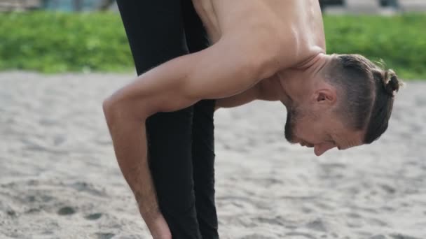 Крупним планом чоловік робить йогу і розтягує вправи на піщаному пляжі . — стокове відео