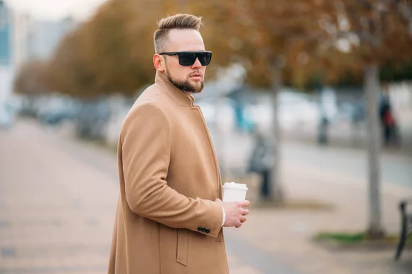 Schöner bärtiger junger Mann mit Sonnenbrille trinkt Kaffee im Park, Kopierplatz auf Tasse — Stockfoto