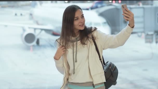 Schöne Frau macht Selfie-Foto in der Nähe des Flughafenfensters im Hintergrund des Flugzeugs — Stockvideo