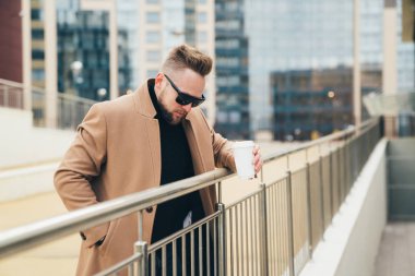 Açık havada korkuluk çekici şık erkek güneş gözlüğü take-away kahve ile eğildi