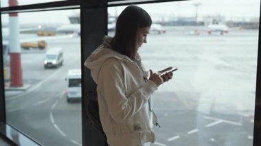 Kadın cep telefonu kullanır ve elini birine havaalanında penceresinden dalgalar.