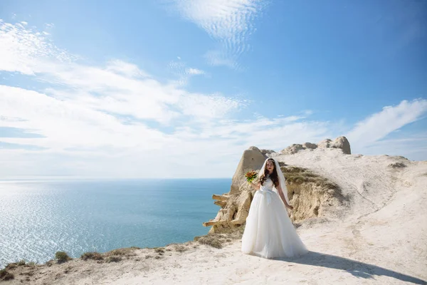 Hermosa novia en vestido blanco se encuentra en el fondo de roca del océano —  Fotos de Stock