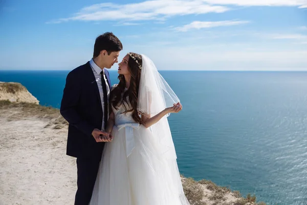 Hermosa pareja de recién casados abrazándose en el día de la boda en el acantilado con vista al mar —  Fotos de Stock