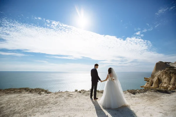 Sposa e sposo sono in piedi sulla scogliera con oceano e cielo blu sfondo nella giornata di sole — Foto Stock