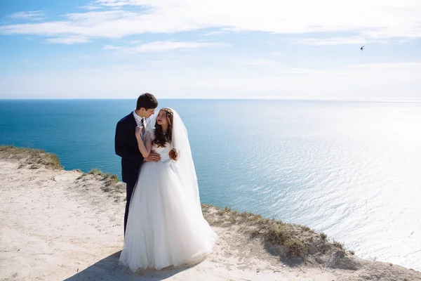 Bella coppia di sposi che si abbracciano il giorno del matrimonio sulla scogliera con vista sull'oceano — Foto Stock