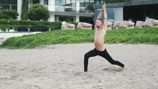 Sportos félmeztelen férfi csinál a nyújtó jóga gyakorlatok, a homokos strand — Stock videók