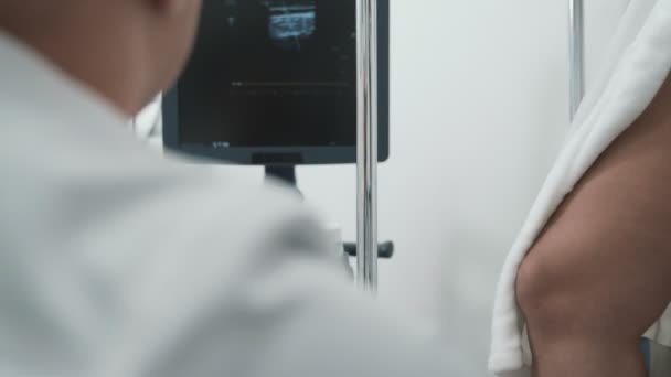 Sicht Arzt macht einen Ultraschall an den Beinen des Patienten und blickt auf den Monitor, Nahaufnahme — Stockvideo