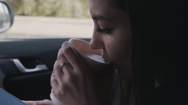 Mooi meisje zit in de auto met kopje koffie in haar handen. — Stockvideo