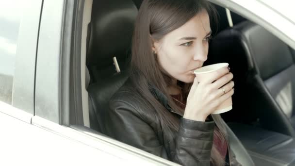 Mooi meisje zit in de auto met kopje koffie in haar handen — Stockvideo