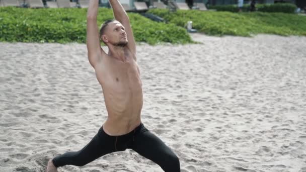 Slow motion steadicam shot, atlético hombre sin camisa haciendo ejercicios de estiramiento en la playa de arena . — Vídeos de Stock