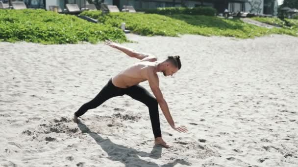Slow motion steadicam shot, atlético hombre sin camisa haciendo ejercicios de estiramiento en la playa de arena . — Vídeos de Stock