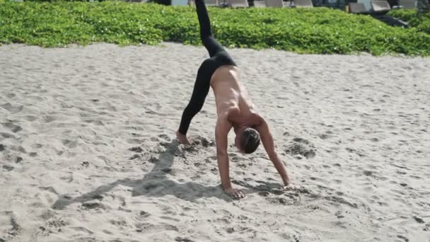 Slow motion steadicam shot, atlético hombre sin camisa haciendo ejercicios de estiramiento en la playa de arena . — Vídeos de Stock
