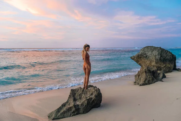 Frau mit perfekt gebräuntem Körper steht bei schönem Sonnenuntergang auf einem großen Stein am Strand — Stockfoto