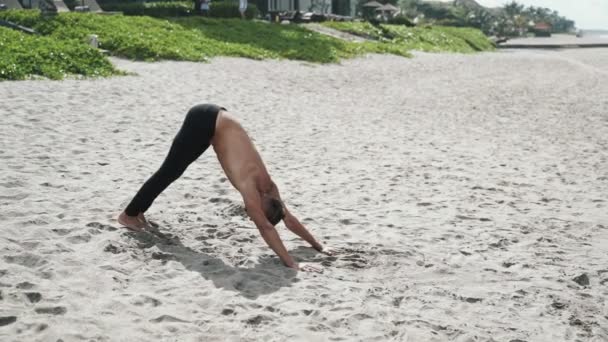スローモーション ステディカム ショット 砂浜のビーチでストレッチ体操を行う運動の上半身裸の男 屋外男性練習ヨガ コンセプト スポーツ フィットネス アクティブなライフ スタイル — ストック動画