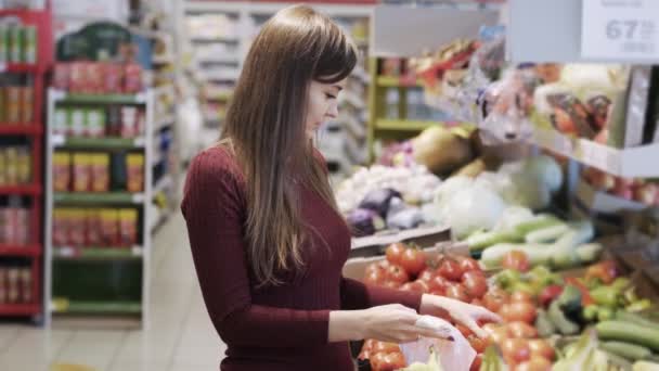 Gadis muda membeli sayuran di departemen supermarket dan menempatkan mereka dalam kantong plastik — Stok Video