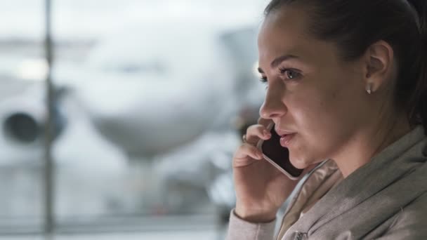 Närbild porträtt av vackra flicka pratar telefon i lounge zon vid flygplatsen på bakgrund av planet — Stockvideo
