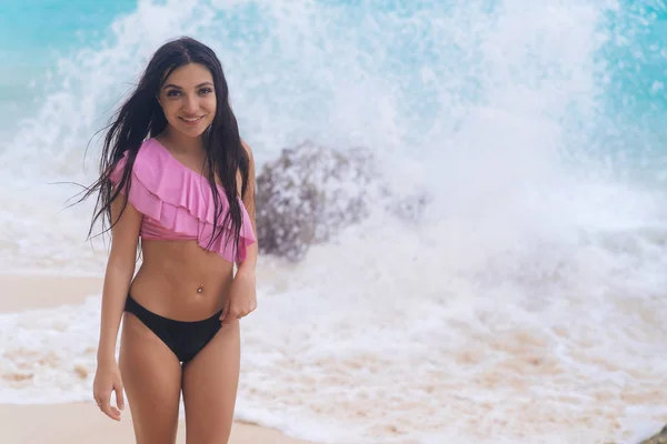 Sexy braungebranntes Mädchen im Badeanzug posiert am Strand in der Nähe des Ozeans mit großen Wellen — Stockfoto