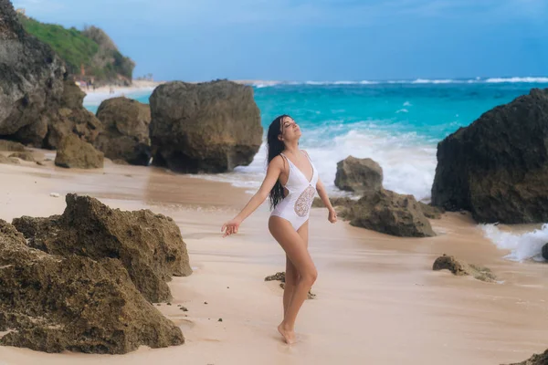 Glückliches Mädchen im Badeanzug mit weit aufgerissenen Armen entspannt sich am Strand mit schönen Wellen auf dem Hintergrund — Stockfoto