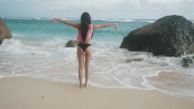 Yavaş hareket ters veiw ince kız mayo ile plajda, geniş açık silah standları görünüyor okyanus dalgaları, steadicam vurdu