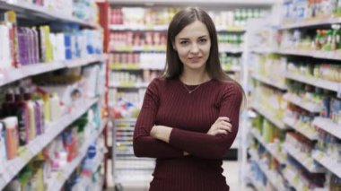 Güzel kadın gülümseyen ve kameraya bakarak süpermarkette rafların arasında duruyor