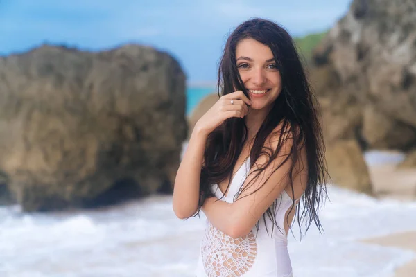 Ritratto di ragazza felice sorridente in costume da bagno bianco sulla spiaggia con sfondo di rocce, grandi pietre e oceano — Foto Stock
