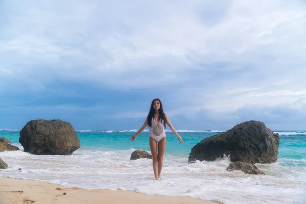Schöne sexy Frau in weißer Badebekleidung posiert und gebräunt im Sommerurlaub am felsigen Strand — Stockfoto