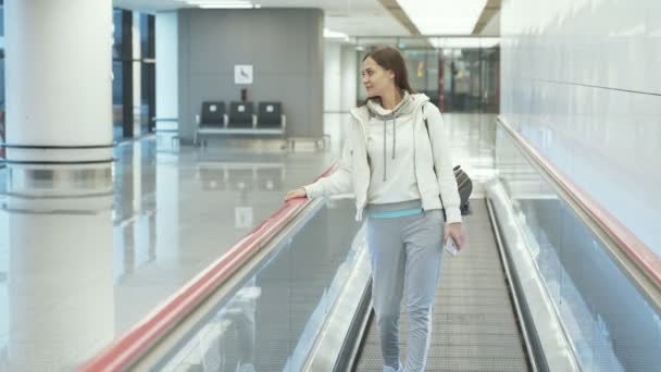 Young woman in sportswear goes on moving walkway at airport — Stock Video