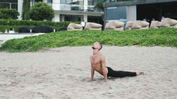Lekkoatletycznego mężczyzna robi pozy i pilates ćwiczenia jogi na plaży — Wideo stockowe