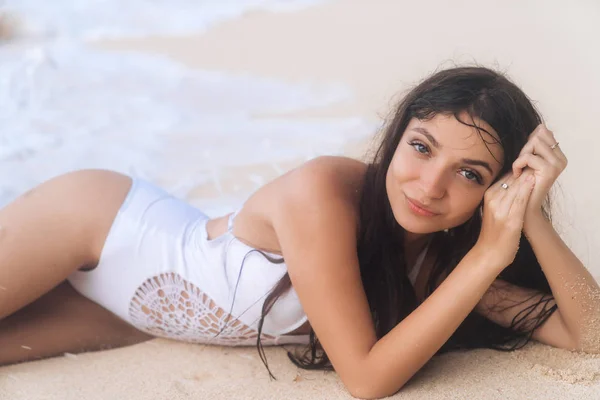 Portret van mooi lachende meisje in witte zwembroek liggend op het strand in golven van de Oceaan — Stockfoto
