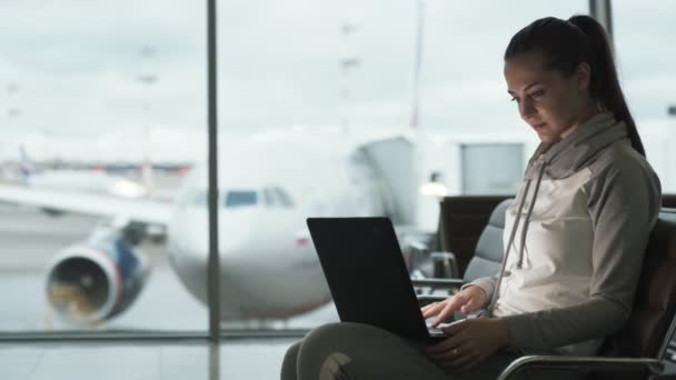 Menina viajante freelancer em sportwear usa laptop para trabalhar no lounge do aeroporto — Vídeo de Stock