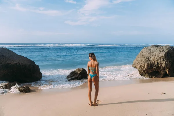 Schlankes Mädchen im Badeanzug posiert am tropischen Strand mit großen Steinen. — Stockfoto