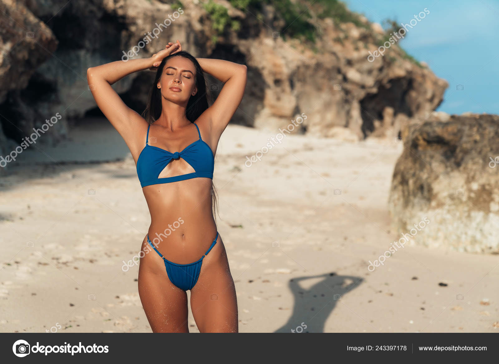 Sexy girl in blue swimsuit sunbathes on the white sand beach