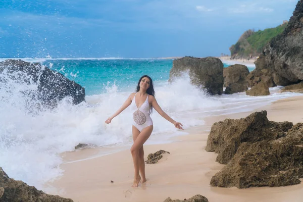 Glückliches Mädchen im Badeanzug mit weit aufgerissenen Armen entspannt sich am Strand mit schönen Wellen auf dem Hintergrund — Stockfoto