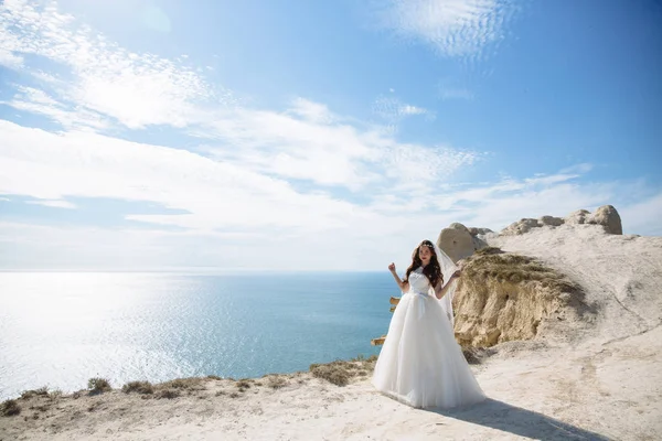 Hermosa novia en vestido blanco se encuentra en el fondo de roca del océano —  Fotos de Stock