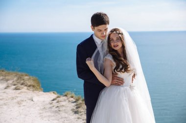 Cliff, düğün gününde newlyweds portresi güzel okyanus manzarasına sahip. Şık elbiseli damat gelin beyaz elbiseli kucaklar. Sadece evli kavramı