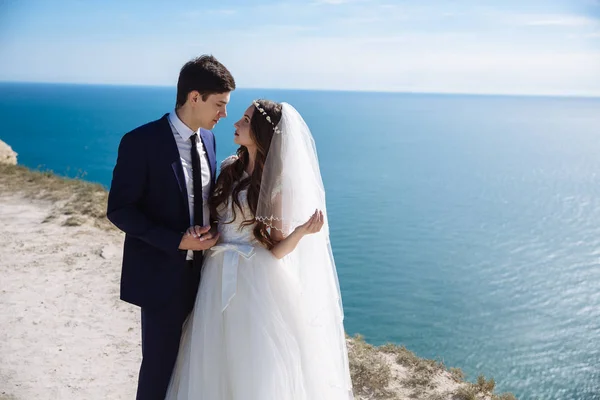 Sposa elegante e sposo elegante guardano l'un l'altro con amore a sparatoria di fotografia su rupe con vista sull'oceano — Foto Stock