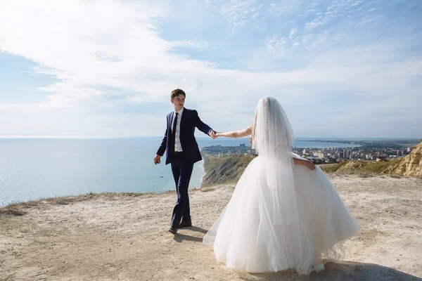 Sposa e sposo si tengono per mano e ballano sulla montagna con vista sull'oceano — Foto Stock