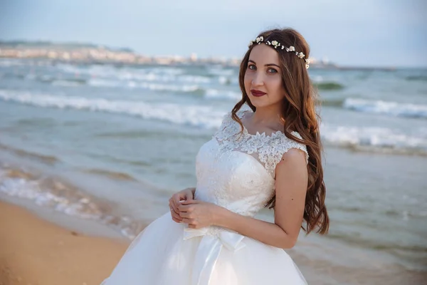 Retrato de novia en vestido de novia con pelo largo rizado y corona de flores en su cabeza en la playa del océano —  Fotos de Stock