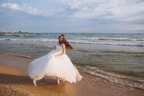 Boldog szép menyasszony, esküvői ruha fényörvények siklanak és táncok a ocean beach — Stock Fotó
