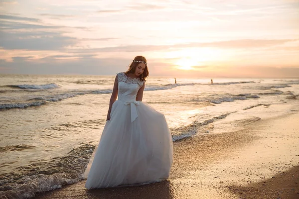 Romantikus menyasszony, fehér ruhában, óceán tengerparti strandon napnyugta időpontja. Fiatal gyönyörű menyasszony az esküvő napján — Stock Fotó