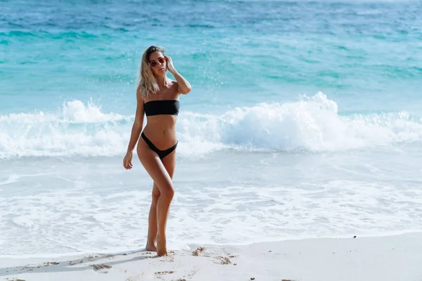 Hermosa chica sexy en traje de baño y gafas de sol que salen del océano a la playa — Foto de Stock
