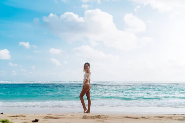 Стройная сексуальная девушка в бежевом топе и в бикини позирует на тропическом пляже — стоковое фото