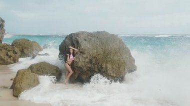 Ağır çekim güzel genç kız mayo ayakta yakınındaki plaj ve arka plan okyanus dalgaları, steadicam vurdu, büyük taş