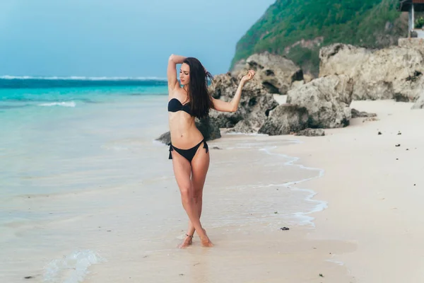 性感晒黑模型在黑色泳衣摆姿势在白色沙滩上 — 图库照片