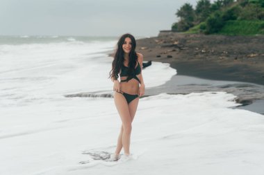 Siyah kum plajı üzerinde poz mayo çekici mutlu kız. Muhteşem vücut okyanus yakın dinlenme ile model