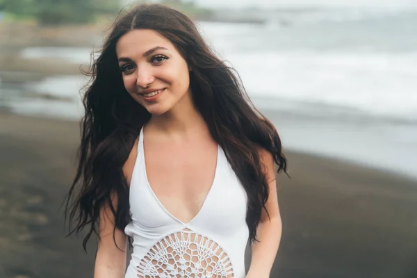 Portrait of young woman in white swimsuit posing on black sand beach. — Stock Photo, Image