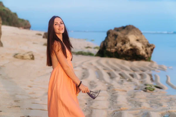 Feliz chica sonriente en vestido de sol y con gafas de sol en la mano descansando en la playa tropical salvaje — Foto de Stock