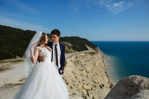 Brudgummen i elegant kostym och bruden i vit klänning på weddingday på klippa med vacker utsikt över havet — Stockfoto